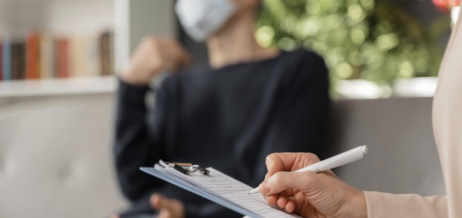 woman-therapist-taking-notes-of-man-in-therapy-office-with-mask-scaled